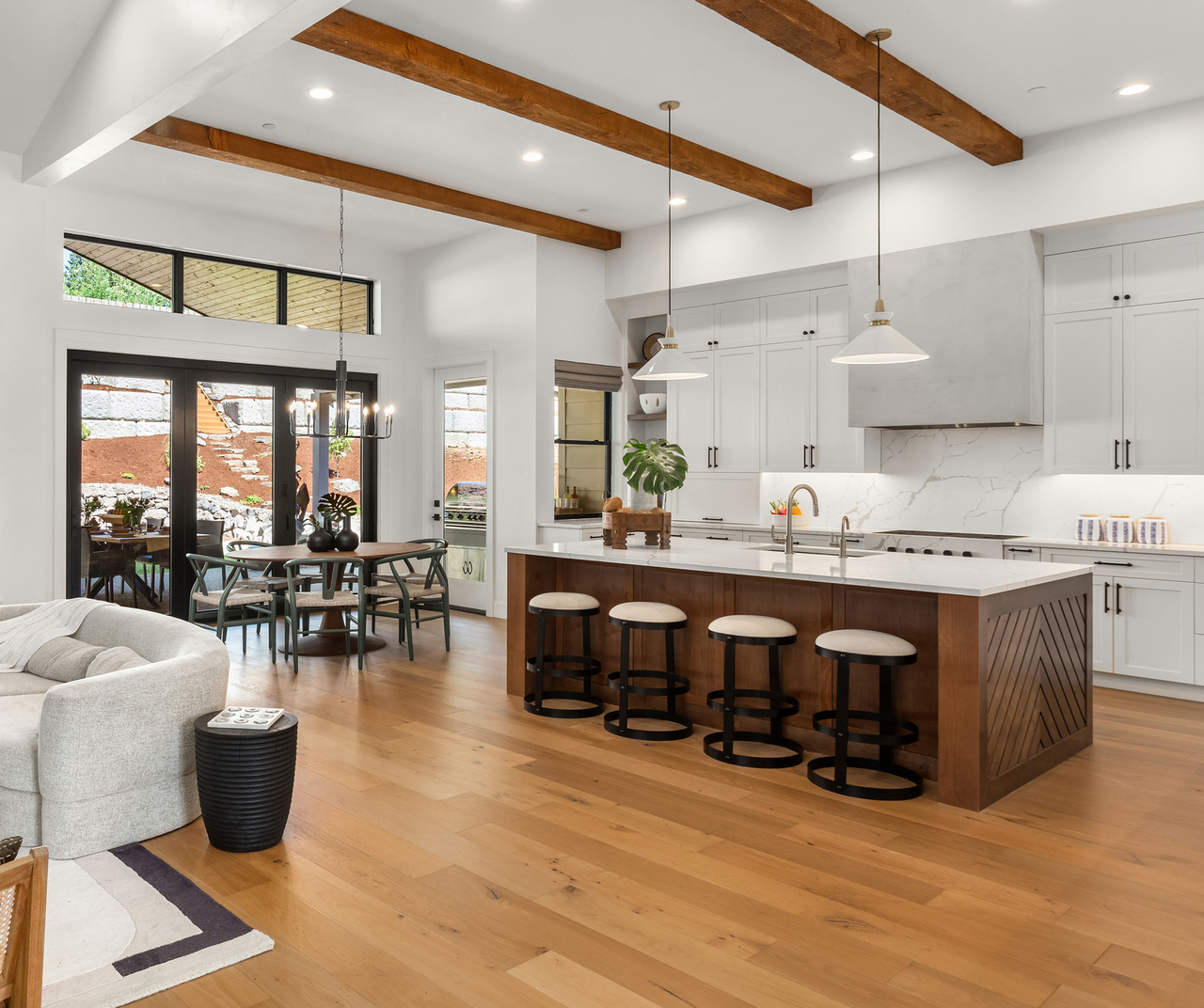 Beautiful living room and kitchen in new luxury home with white cabinets, wood beams, pendant lights and hardwood floors